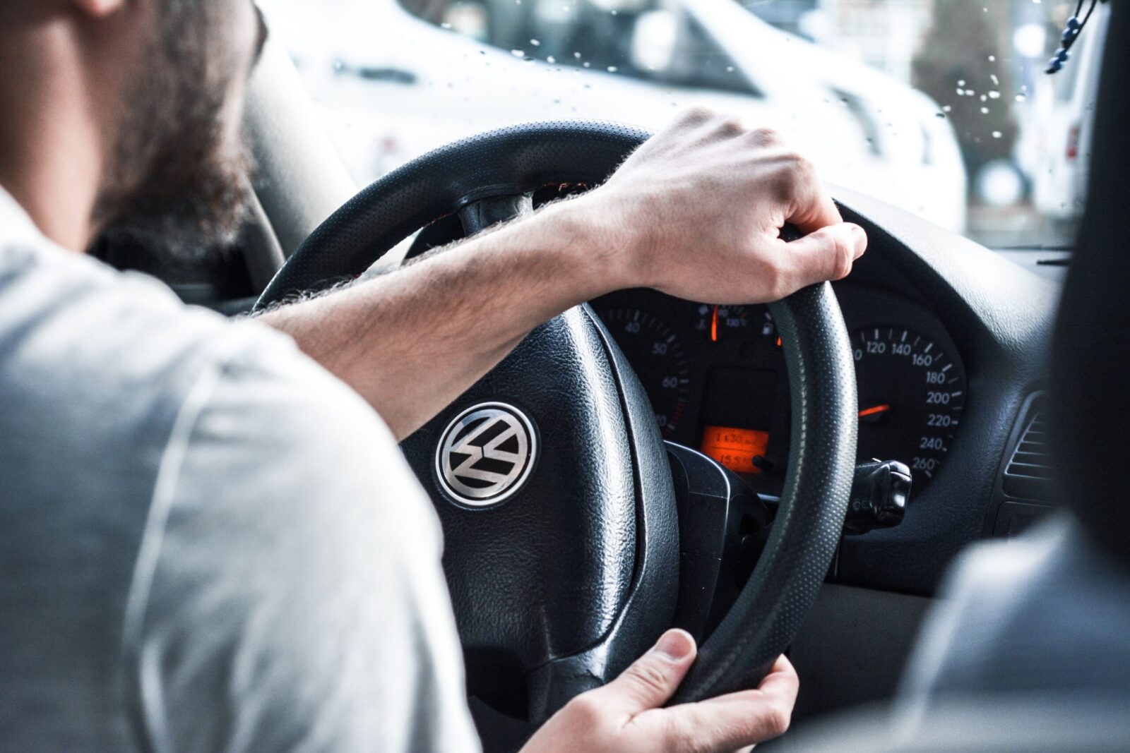 Man gripping Volkswagen steering wheel, focused on driving and vehicle interior details.